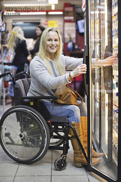 Porträt einer glücklichen behinderten Frau im Rollstuhl im Kühlregal des Supermarktes