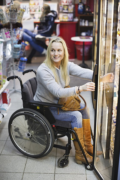 Glückliche behinderte Frau im Rollstuhl im Kühlbereich des Supermarktes schaut weg