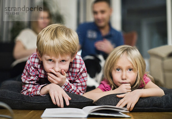 Porträt von kleinen Geschwistern mit Buch auf der Vorderseite und Eltern im Hintergrund