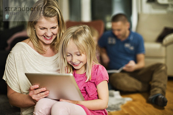 Mutter und Tochter mit digitalem Tablett mit Familie im Hintergrund