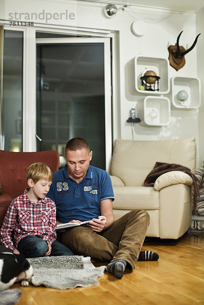 Vater und Sohn beim Lesen des Buches auf dem Boden im Wohnzimmer