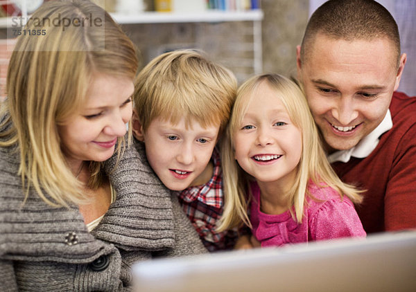 Porträt eines glücklichen Mädchens mit Familie  das den Laptop zu Hause benutzt.