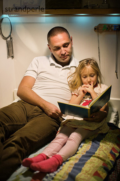 Vater und Tochter lesen gemeinsam im Bett.