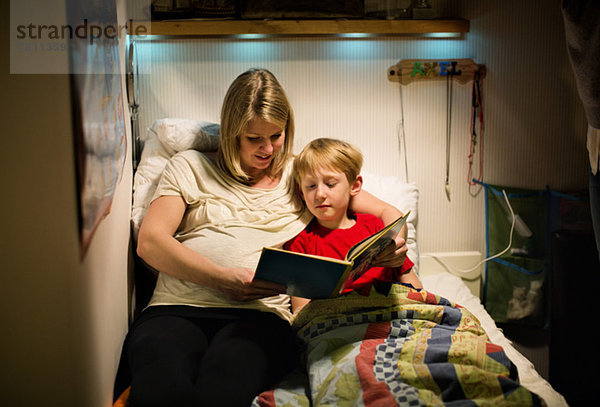 Mutter und Sohn lesen gemeinsam im Bett.