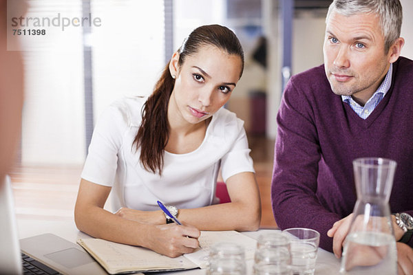 Geschäftsfrau macht sich Notizen  während sie mit Kollegen in einer Besprechung sitzt.