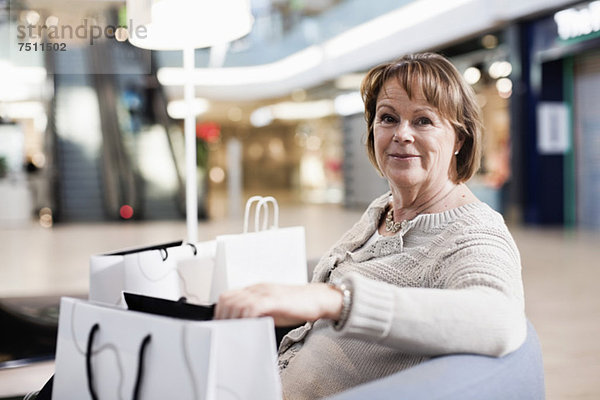 Fröhliche Seniorin mit Einkaufstaschen auf dem Sofa im Einkaufszentrum