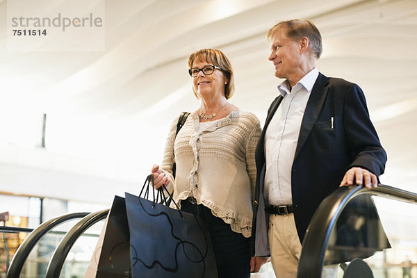 Glückliches Seniorenpaar mit Taschen auf einer Rolltreppe im Einkaufszentrum