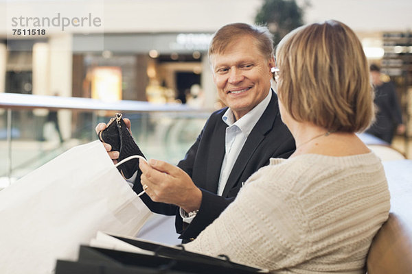 Glücklicher älterer Mann  der seine Einkäufe der Frau im Einkaufszentrum zeigt.