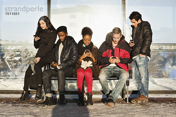 Gruppe von ethnischen Freunden  die Mobiltelefone auf der Bank benutzen.