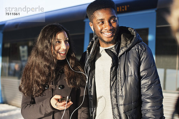 Fröhliche junge Freunde hören Musik durch Freisprecheinrichtung gegen den Zug