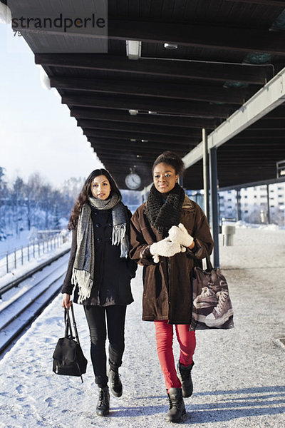 Junge Freundinnen in warmer Kleidung  die auf dem Bahnsteig laufen.