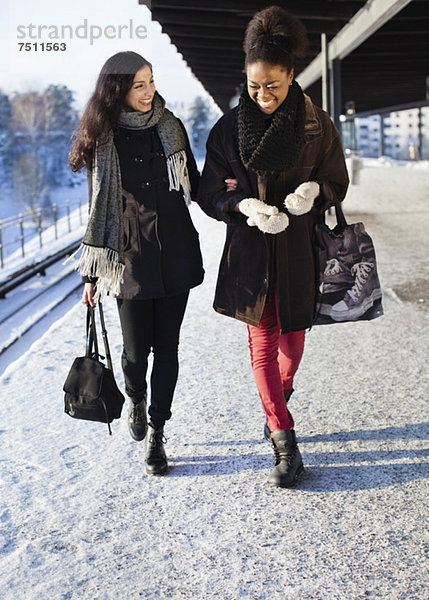 Fröhliche Freundinnen in warmer Kleidung auf dem Bahnsteig