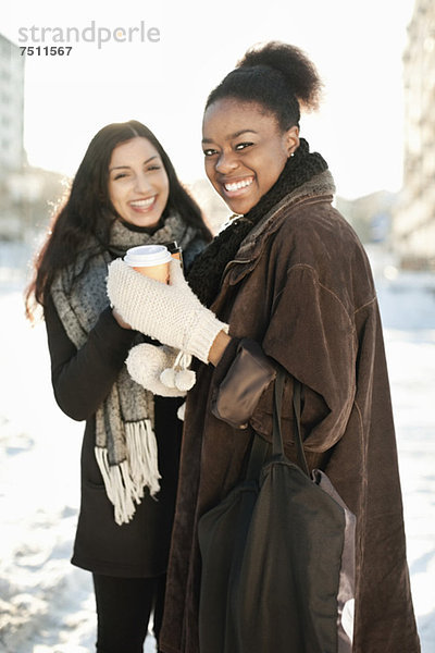 Portrait von glücklichen Freundinnen in warmer Kleidung mit Einwegbechern