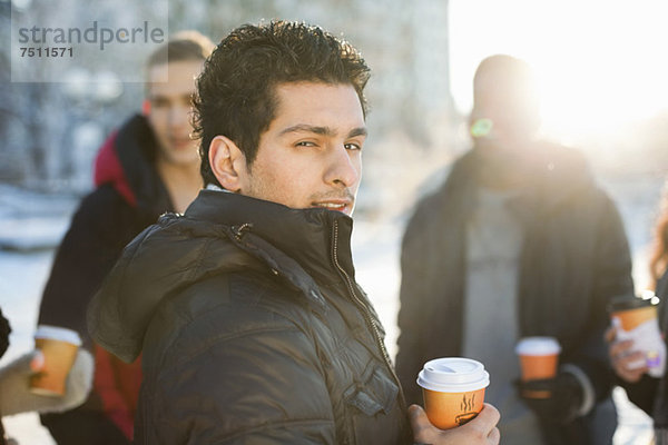 Portrait eines jungen Mannes mit Freunden in warmer Kleidung mit Einwegbechern