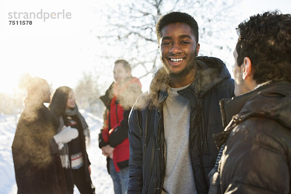 Junge Männer in warmer Kleidung mit Freunden kommunizieren im Hintergrund