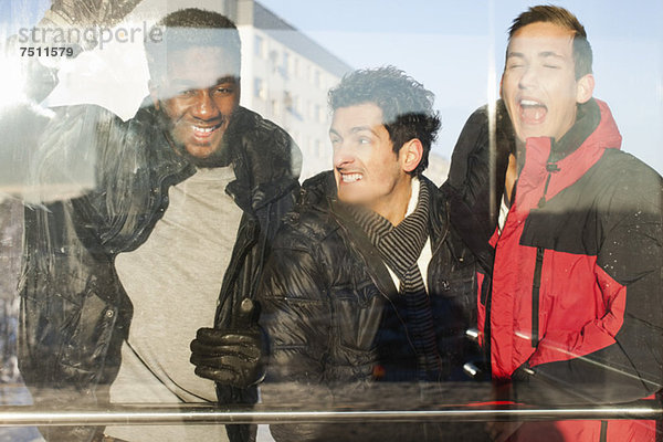 Verspielte männliche Freunde in warmer Kleidung  die gegen Glas stehen