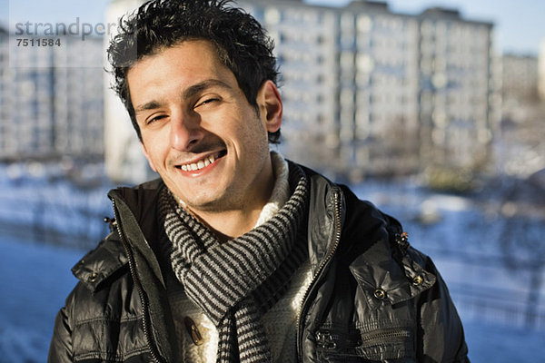 Porträt eines glücklichen jungen Mannes in Schalldämpfer und Jacke mit Gebäuden im Hintergrund
