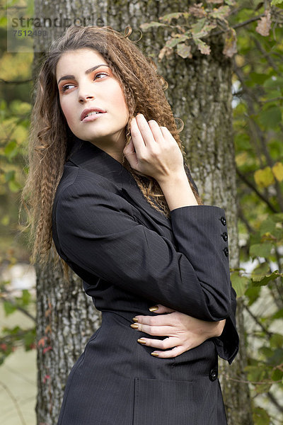 Junge Frau mit langen Haaren und schwarzem Blazer vor einem Baum