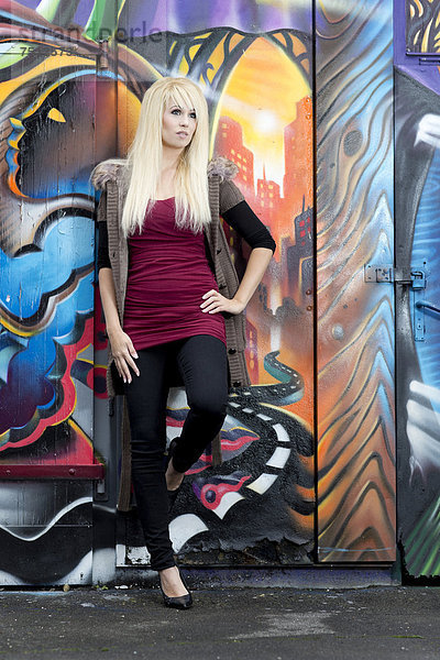 Junge Frau mit langen blonden Haaren posiert vor Wand mit Graffiti