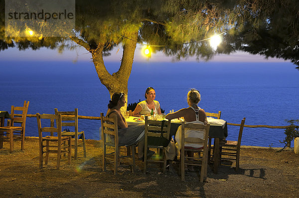 Drei Frauen sitzen abends an einem Tisch unter einem Baum  Abendstimmung in einem griechischen Garten am Meer  Lefkas  Griechenland  Europa