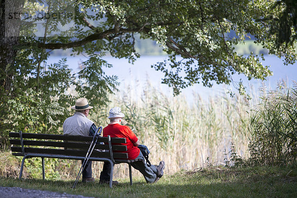 Ein älteres Paar sitzt auf einer Bank am Seeufer  Weißensee  Kärnten  Österreich  Europa Symbolbild.