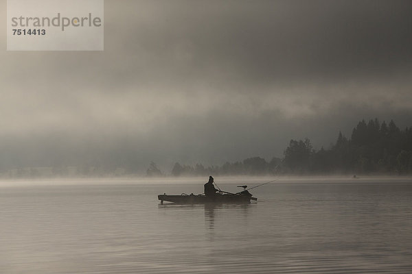 Angler früh am Morgen mit Nebel im Morgenlicht auf dem Weißensee  Kärnten  Österreich  Europa