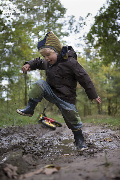 Ein kleiner Junge springt mit Freude in eine Pfütze während eines Herbstspaziergangs  Brandenburg  Deutschland  Europa