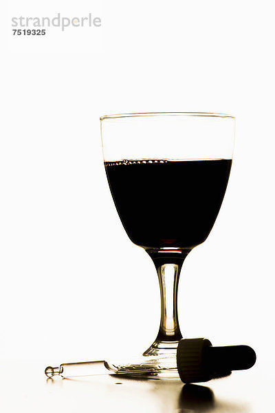 Eine Pipette liegt neben einem Glas Rotwein