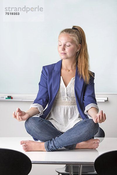 Geschäftsfrau sitzt barfuß in einer Yoga-Position auf ihrem Schreibtisch