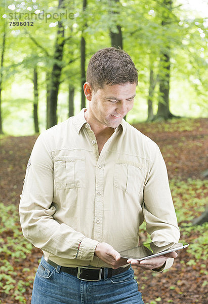 Ein Mann steht im Wald und schaut auf seinen Tablet-PC