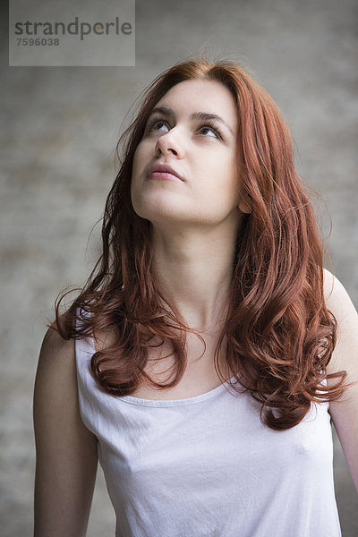 Nachdenkliche junge Frau mit roten Haaren blickt nach oben