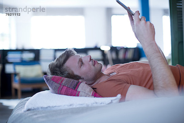 Mann mit digitalem Tablett auf dem Bett