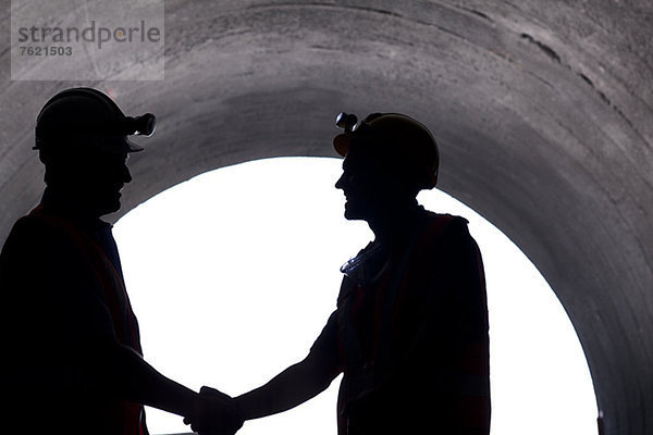 Silhouette der Arbeiter beim Händeschütteln im Tunnel