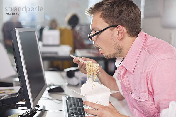 Geschäftsmann isst chinesisches Essen am Schreibtisch