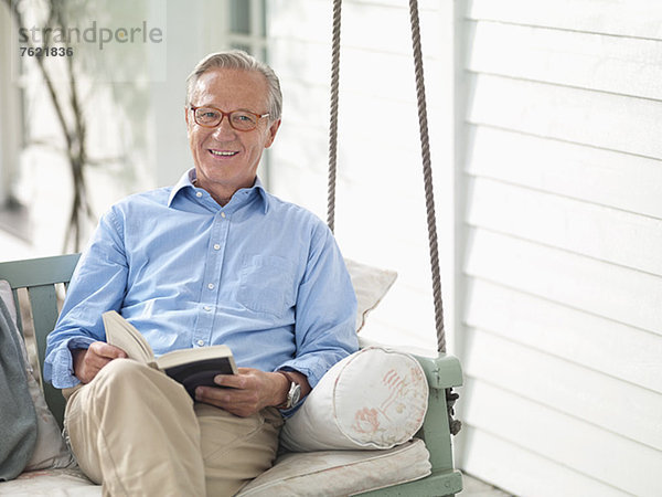Mann liest Buch auf Veranda-Schaukel