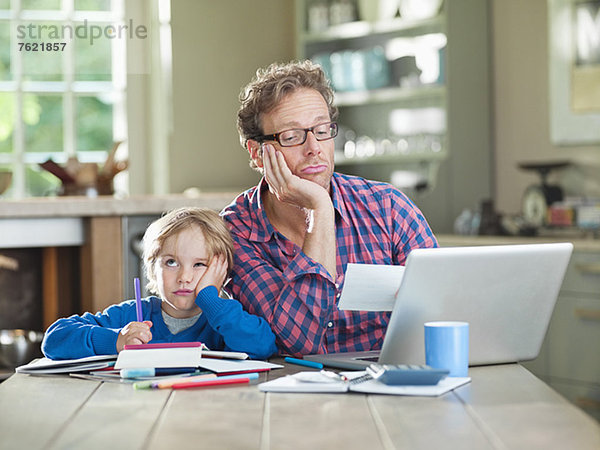 Gelangweilter Vater und Sohn bei der Arbeit am Tisch