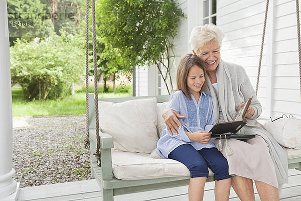 Frau und Enkelin beim Lesen auf der Veranda-Schaukel