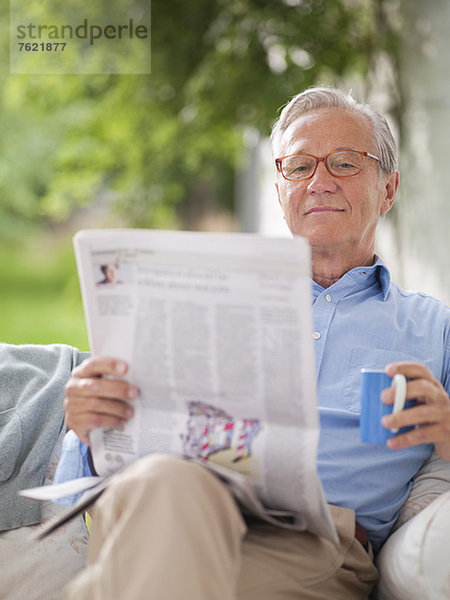 Mann liest Zeitung in Veranda-Schaukel