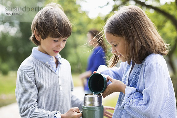 Kinder beim Ausgießen von Tee aus der Thermoskanne im Freien