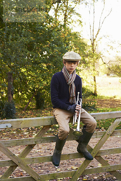 Teenager-Junge hält Trompete auf Holzzaun