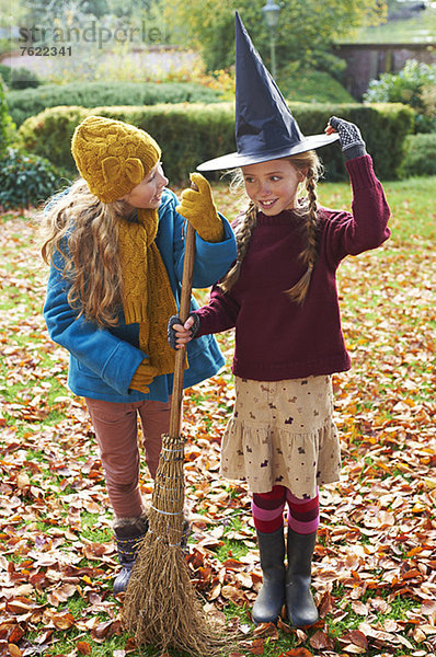 Mädchen beim Spielen mit Hexenhut und Besen im Freien
