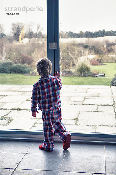 Junge im Pyjama mit Blick aus dem Fenster