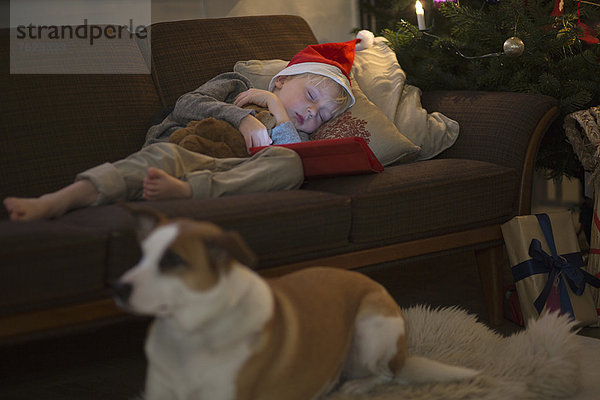 Junge mit Nikolausmütze schläft auf dem Sofa