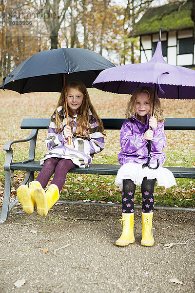 Mädchen in Regenstiefeln und Regenschirmen im Park
