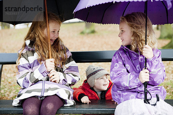 Mädchen mit Regenschirmen auf Parkbank