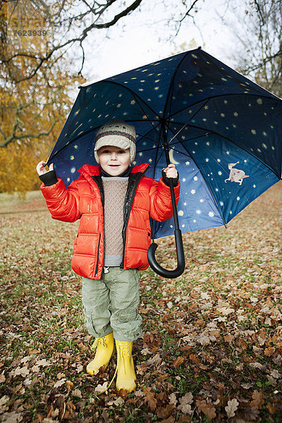 Junge in Regenstiefeln und Regenschirm im Park