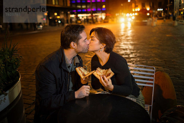 Küssendes Paar beim Pizza essen im Freien