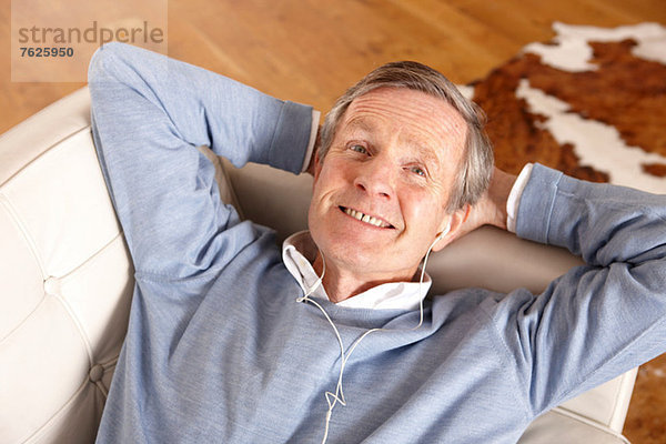 Älterer Mann hört Kopfhörer auf dem Sofa