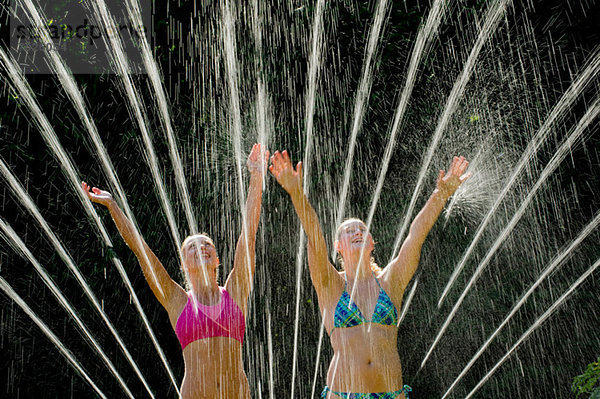 Teenager-Mädchen spielen in Sprinkleranlagen