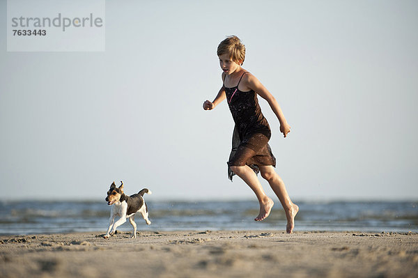 Mädchen läuft mit einem Dansk-Svensk Gardshund am Strand